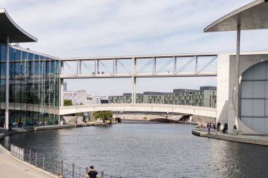 Berlin, Almanya - 1 Eylül 2025: Berlin 'de insanlar modern mimariye hayran kalarak kanal boyunca yürüyorlar. Köprüler her iki tarafı birbirine bağlar, güneşli bir günde canlı bir şehir atmosferi yaratır..