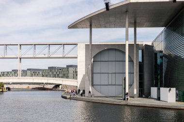 Berlin, Almanya - 1 Eylül 2025: Berlin 'in mimari manzarası Spree Nehri boyunca modern binaları vurguluyor. İnsanlar açık havada mavi gökyüzüyle deniz kenarında gezinir, manzaranın tadını çıkarırlar..