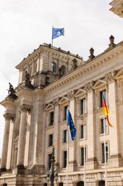 Berlin, Almanya - 1 Eylül 2025: Almanya ve Avrupa Birliği bayrakları Berlin 'deki tarihi Reichstag binasının tepesinde dalgalanmaktadır. Turistler açık mavi gökyüzü altındaki mimariye hayran.