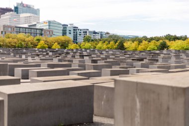 Berlin, Almanya - 1 Eylül 2025: Ziyaretçiler, büyük beton bloklarla işaretlenmiş önemli bir alan olan Berlin Soykırım Anıtı 'nı keşfediyorlar. Çevreleyen ağaçlar canlı sonbahar yapraklarını sergiler
