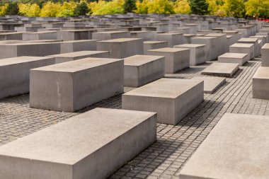 Berlin, Almanya - 1 Eylül 2025: Ziyaretçiler, Berlin 'deki soykırım anıtının ağaçlarla çevrili beton levhalarının arasında yürüyorlar. Temiz gökyüzü, anıların kutsal atmosferini güçlendiriyor..