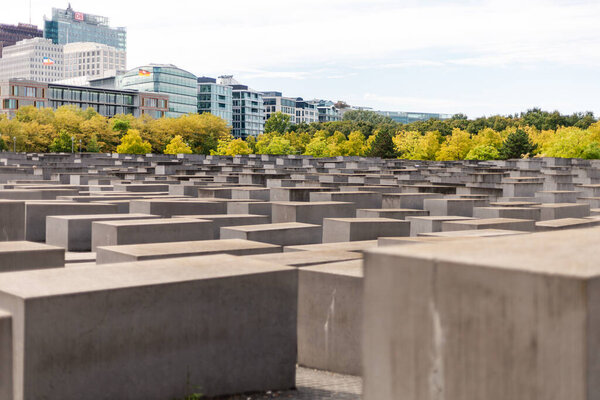 Берлин, Германия - 1 сентября 2025 года: Посетители изучают Мемориал Холокоста в Берлине, значительное место, отмеченное большими бетонными блоками. Окружающие деревья демонстрируют яркую осеннюю листву