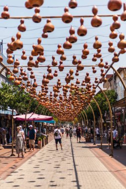 Alanya, Türkiye - 10 Temmuz 2025: Alanya 'daki canlı bir caddede, insanlar canlı pazarda yürürken yukarıda asılı duran bir dizi su kabağı bulunuyor. Gölgeli tezgahlar yerel mal ve el sanatları sunuyor