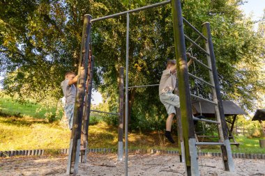 İki çocuk doğal ortamda neşeyle oynuyorlar, oyun parkına tırmanıyorlar ve güneşli bir günde dışarıda eğleniyorlar..