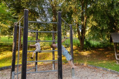 İki çocuk dışarıda eğleniyor. Parktaki bir oyun parkına tırmanıyorlar. Ağaçların arasında oynarken ve keşfederken temiz hava ve güneşin tadını çıkarırlar..