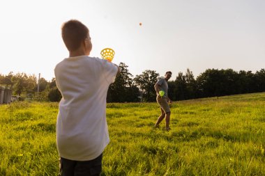 Bir baba ve oğul, güneşli bir tarlada bir ileri bir geri top atarak doğada kaliteli zaman geçirirler. Uzun otlar ve ağaçlar eğlenceli öğleden sonraları için sıcak bir atmosfer yaratıyor..