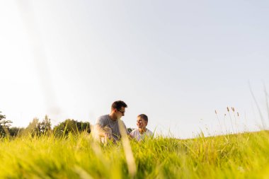 Bir baba ve oğlu yemyeşil bir tarlada oturuyor, birlikte gülüyor ve gülüyorlar. Güneşli güzel bir günün tadını çıkarıyorlar, doğayı kucaklıyorlar ve birbirlerine eşlik ediyorlar..