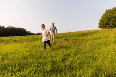 Bir baba ve oğul yemyeşil bir tarlada birlikte koşarken gülüyorlar. Sıcak güneş ışığı sahneyi yıkıyor, neşeli bir bağlantı ve macera atmosferi yaratıyor..