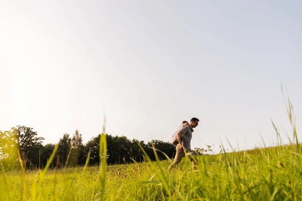 Babam yemyeşil bir tarlada yürürken oğlunu sırtında taşır. Sıcak bir öğleden sonra, açık bir gökyüzünün altında ağaçlarla çevrili neşeli bir anı paylaşıyorlar..