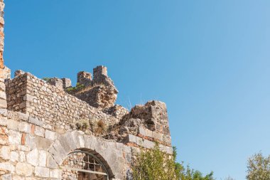 Parlak mavi gökyüzüne karşı yükselen tarihi bir taş yapısının kalıntıları antik zanaatkarlığı ve doğanın güzelliğini vurguluyor..