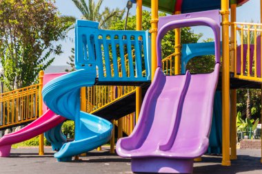 Çocuklar güneşli bir öğleden sonra yeşilliklerle çevrili parlak bir oyun alanında renkli slaytlarda oynayarak eğlenebilirler..