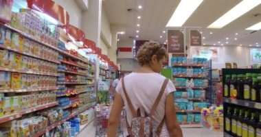 Kadın süpermarkette alışveriş. Dikkatle analiz ürünleri bir pazarda sepeti alışveriş merkezinde genç kadınla geri ateş izleyin.