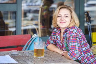 Bir bardak bira ile bir kafede bir masada oturan kısa sarı saçlı Genç Sevimli gülümseyen kız portresi yakın çekim