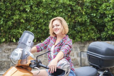 Yakın çekim kısa sarı saçlı bir motosiklet üzerinde oturan ve gülümseyen bir genç Sevimli motorcu kız portresi