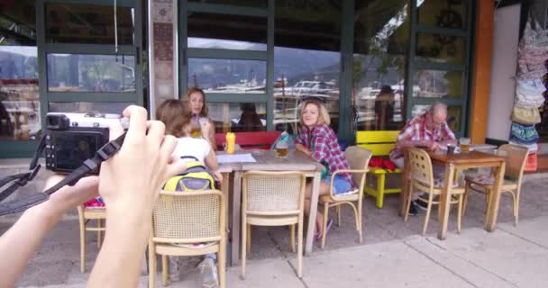 摄影师拍摄年轻美女的照片 她们坐在咖啡馆的桌子旁 喝啤酒聊天 我们可以看到摄影师的手和相机的展示 — 图库视频影像