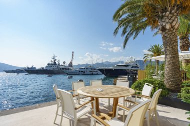 Tivat, Karadağ, 28 Ağustos 2018: Sahil deniz üzerinde bir boş açık kafe tablo. Arka planda gemiler ve yatlar marinada demirlemiş görebilirsiniz