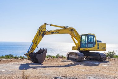 Adriyatik Denizi kıyısında inşaat alanında bir güneşli bahar gününde. Ön planda yerde kazılar bir ekskavatör ve arka planda mavi deniz görebilirsiniz