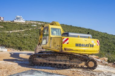 Adriyatik Denizi kıyısında inşaat alanında bir güneşli bahar gününde. Ön planda yerde kazılar bir ekskavatör ve arka planda dağ görebilirsiniz
