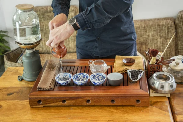 Chinese tea tasting in the tea shop. Tea seller, dressed in European, brews Chinese tea for tasting. Chinese tea set, close-up traditional Chinese teapot and cups on bamboo mats