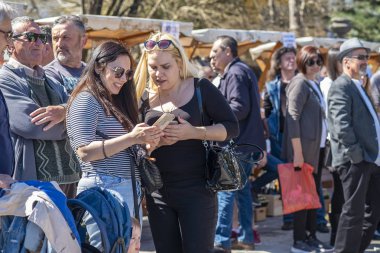 Virpazar, Karadağ, Mart, 24, 2019: karadağlı kasabasında Virpazar 'da şarap ve balıkların kamu Şenliği. İnsanlar kutlamak, parkta yürümek ve yerel müzikal grupların şarkıları dinlemek. İki kadın cep telefonu fotoğrafları bakmak