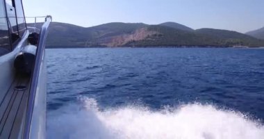 Lüks yat denize açılıyor, büyük köpüklü dalgalar yat omurgave yanlarından ayrılıyor. Dağlar tahtadan görülür