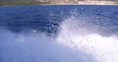 Lüks yat denize açılıyor, büyük köpüklü dalgalar yat omurgave yanlarından ayrılıyor. Dağlar tahtadan görülür