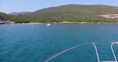 Lüks yat denize açılıyor, büyük köpüklü dalgalar yat omurgave yanlarından ayrılıyor. Dağlar tahtadan görülür