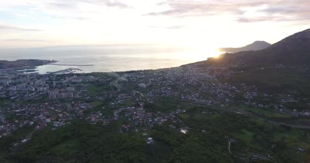 Lotnicze quadcopter strzał z zielonego czarnogórskiego miasta Bar, leżącego na wybrzeżu Adriatyku, o zachodzie słońca na wiosną. Góra w tle — Wideo stockowe
