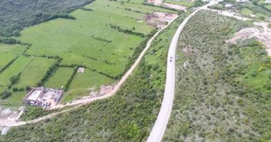 Dağ vadisinde quadcopter uçuşu. Yeşil alanların görünümü, küçük bir köyün çatıları ve yolda seyahat eden araba ve diğer ulaşım ile sarma yolları