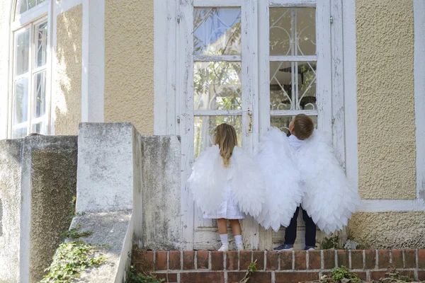 Anak-anak muda berpakaian seperti malaikat berdiri di depan pintu tertutup Stok Gambar Bebas Royalti