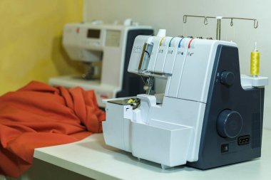 Endüstriyel dolaba yakın çekim, içine bir makara sarı iplik sıkıştırılmış, turuncu bir bez parçası ve arka planda başka bir dikiş makinesi. 