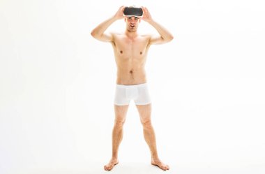 Sanal gerçeklik kulaklığı takmış genç bir adamın tam boy portresi. VR gözlüklü yakışıklı bir erkek. Erkek donu giyen seksi adam. Beyaz boxer şortlu çıplak adam. Erkek iç çamaşırı modası. Satışlar ve indirim