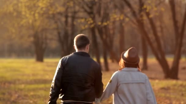 Nettes Paar spaziert im Park der Ruhe bei Sonnenuntergang. Ein Mädchen wirft bei einem Spaziergang einen Hut — Stockvideo