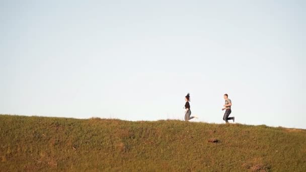 Pareja cariñosa corre alrededor de la colina en un día soleado. Pasar tiempo juntos en la naturaleza — Vídeos de Stock