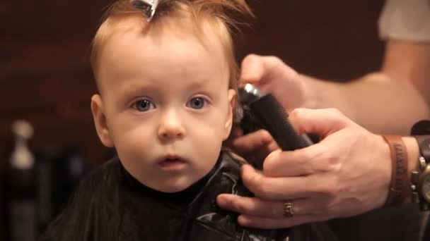 En una peluquería brutal, un niño pequeño está siendo esquilado por un cortador — Vídeo de stock