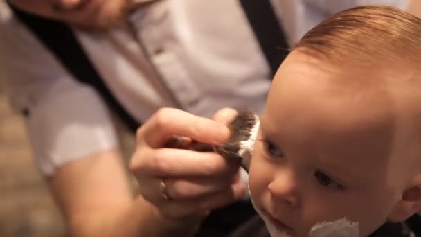 In de schoonheidssalon brutale mens wordt een klein kind toegepast op het scheerschuim van het gezicht met een borstel — Stockvideo