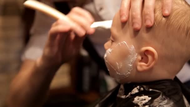 En un brutal salón de belleza para hombres se afeita a un niño pequeño. — Vídeo de stock