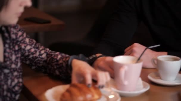 Älskande par handbojor av handbojor äter en croissant och dricker kaffe på ett kafé — Stockvideo