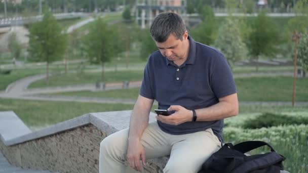 Een man zit in het Park op een groene achtergrond, een onbekende steelt zijn tas en loopt weg — Stockvideo