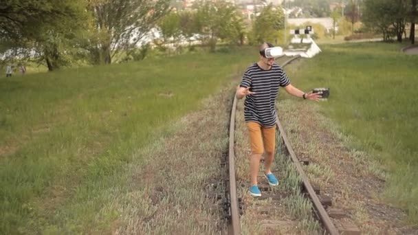 Un joven está en las vías para el transporte ferroviario en un casco de realidad virtual.Ver imágenes, videojuegos.El mundo de la realidad virtual — Vídeo de stock