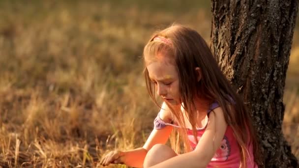 Een schattig klein meisje spelen in een park aan de natuur is boos en huilen vergadering onder een boom — Stockvideo