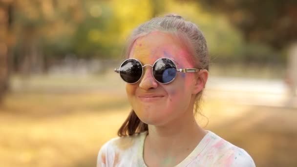 La fiesta de los tintes de color holi. Una chica con gafas levanta un polvo de color azul en el aire. Diversión en el parque de recreo — Vídeo de stock