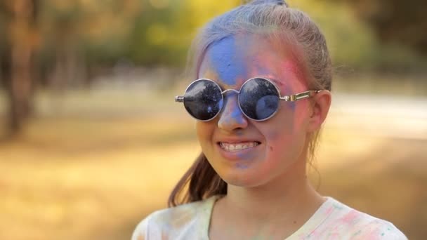 彩画节日。一个戴眼镜的女孩向空气中升起一粒蓝色的彩色粉末。娱乐公园的乐趣 — 图库视频影像