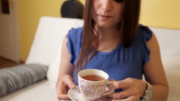 Mladá dívka v modrém obleku a sedí na gauči a pije čaj myšlení o něčem. Pití čaje — Stock video