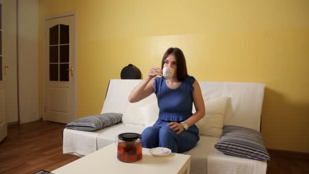 Egy fiatal lány, egy kék színű ül a kanapén, gyorsan teát iszik, hogy elkéstem a munka és menekül — Stock videók