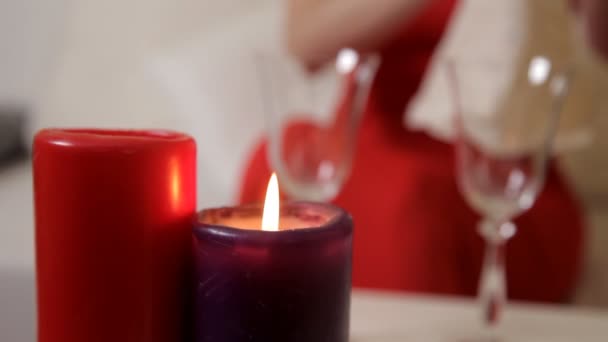 Дівчина в червоній сукні сидить за столом при свічках і п'є шампанське зі склянки — стокове відео