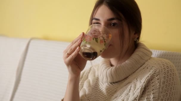 A young girl in a cozy warm sweater on a winter evening at home drinking tea and thinking about something — Stock Video
