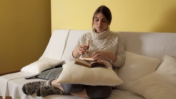 Young girl in a cozy warm sweater at a winter evening at home, putting on glasses reading a book. Winter. House. Girl. Evening.Book — Stock Video