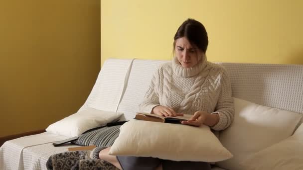 Young girl in a cozy warm sweater at a winter evening at home, putting on glasses reading a book. Winter. House. Girl. Evening.Book — Stock Video