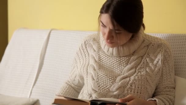 Chica joven en un suéter cálido y acogedor en una noche de invierno en casa, poniéndose gafas de lectura de un libro. El invierno. Casa. Una chica. Buenas tardes. Libro — Vídeos de Stock